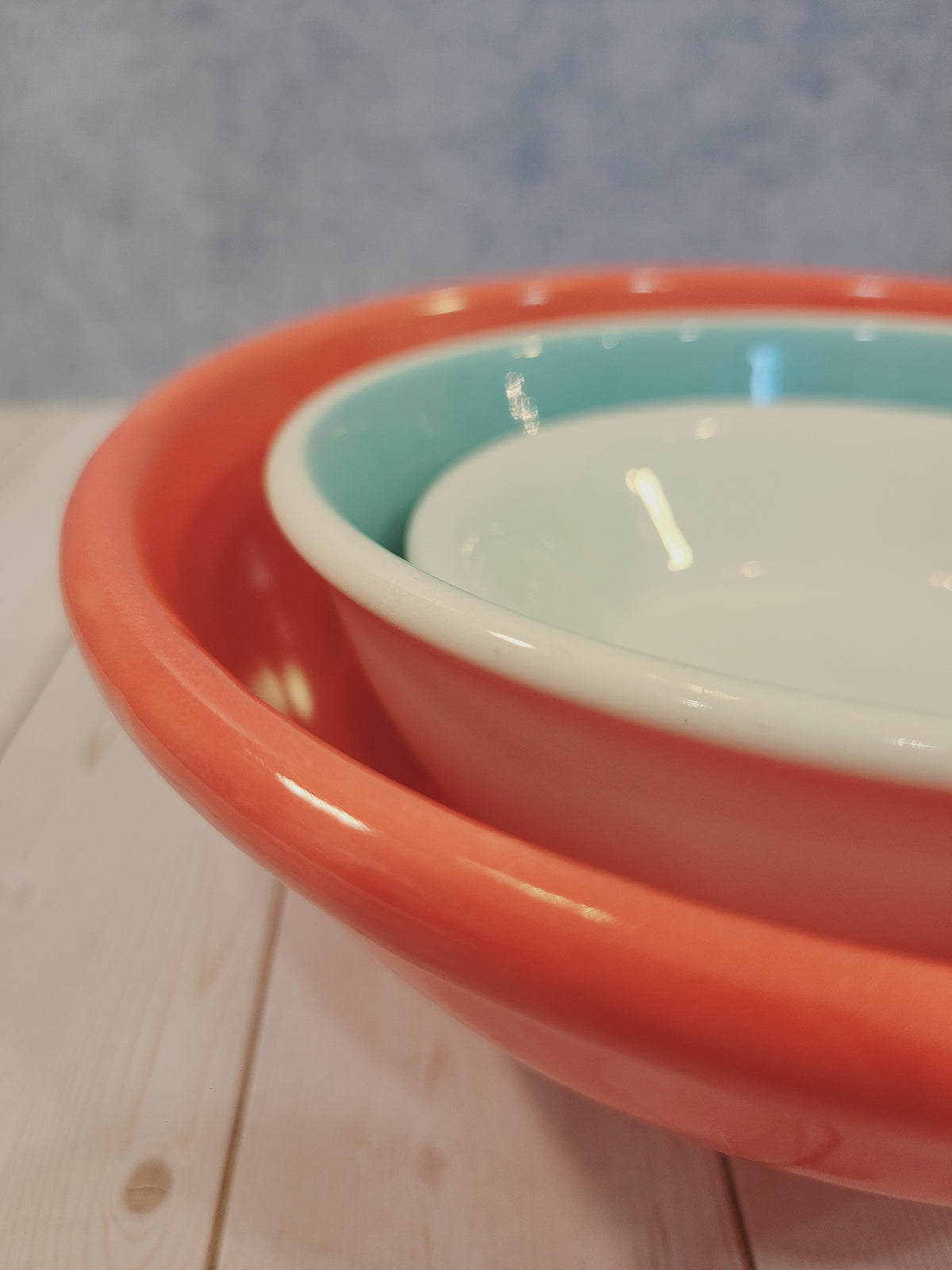 Mid-century American coral utility bowl nested with aqua and white bowls, angled view — vintage USA ceramic kitchenware set