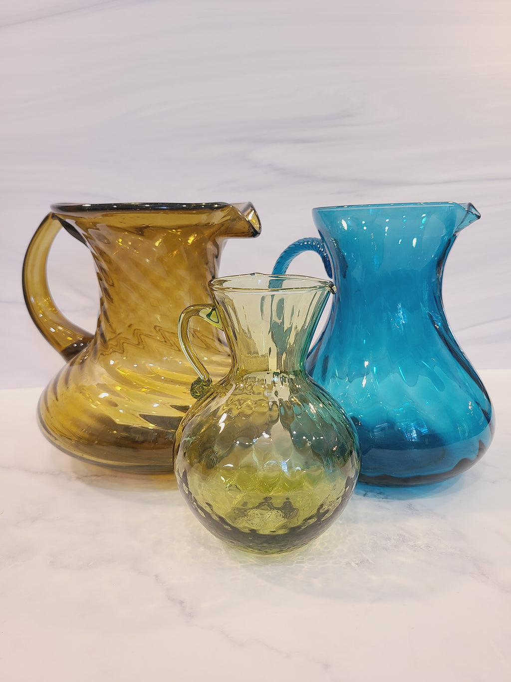 Petite olive green handblown optic glass pitcher displayed with an amber glass pitcher and teal glass pitcher