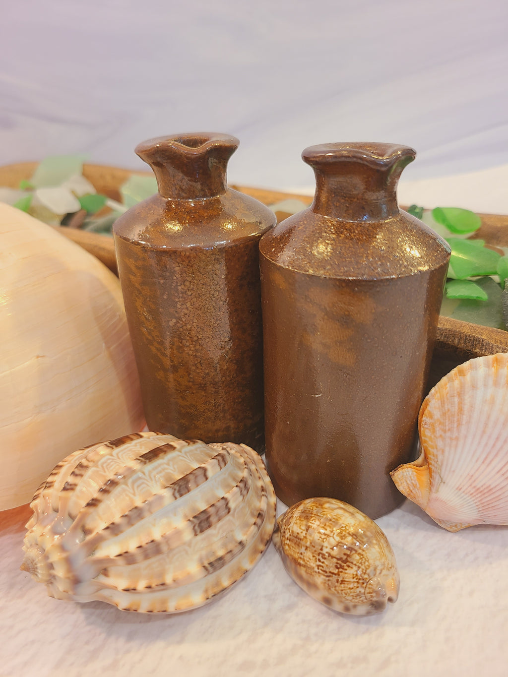 Antique salt-glazed stoneware ink bottles styled in coastal vignette with shells and sea glass — coastal cottage decor
