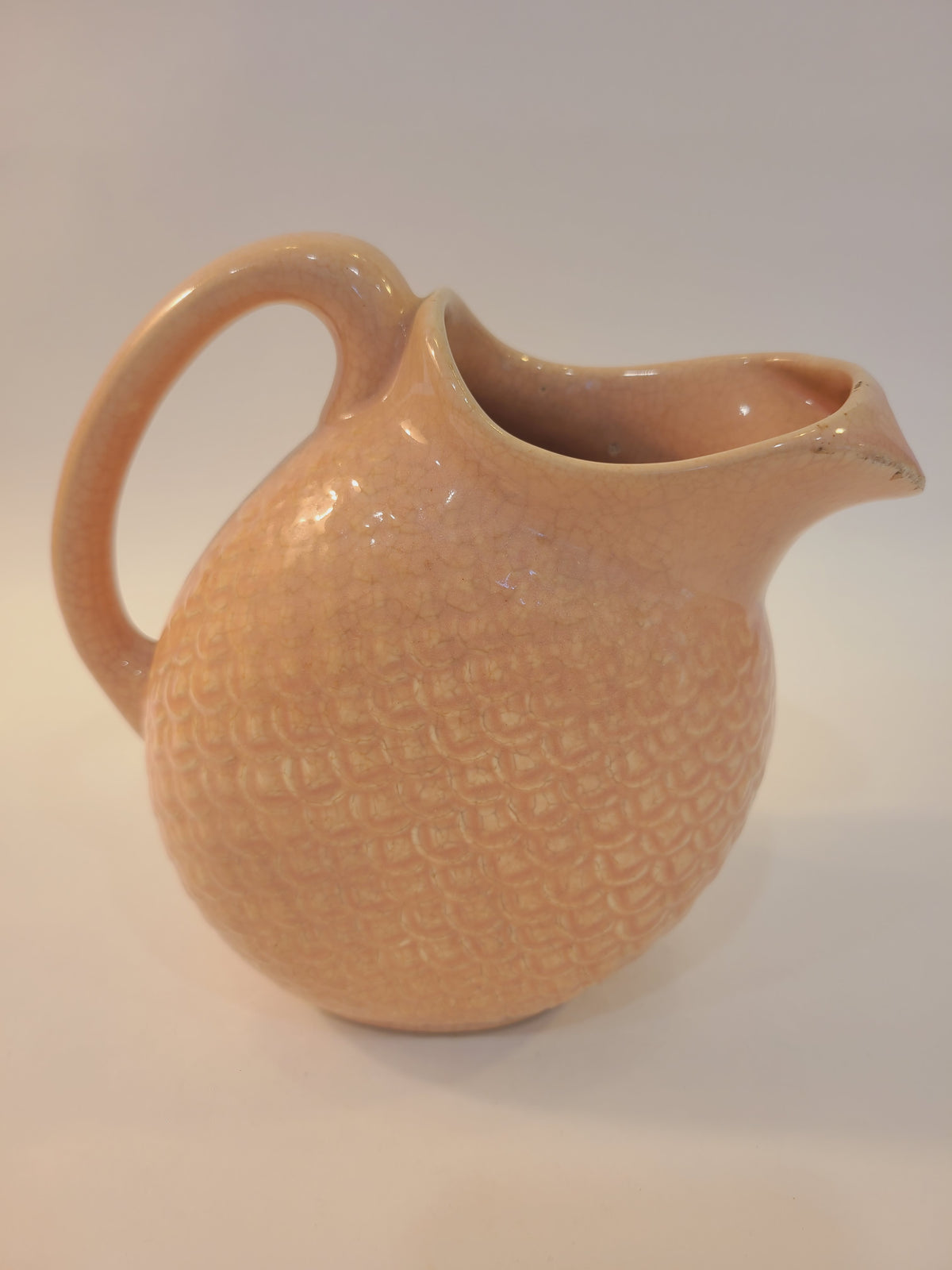 Hull Pottery Nuline Bak-Serve blush pink ceramic pitcher, front three-quarter view, fish scale texture and ice-catcher spout, 1937 American pottery