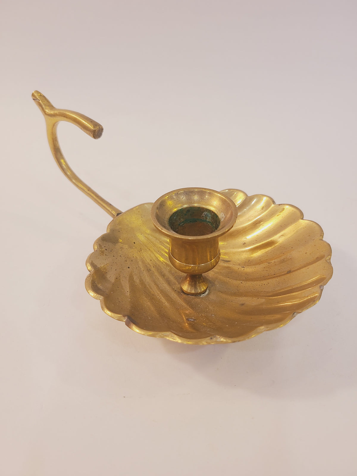 Solid brass shell motif chamber candlestick angled view, scalloped saucer base with taper candle cup and finger loop handle, coastal decor India