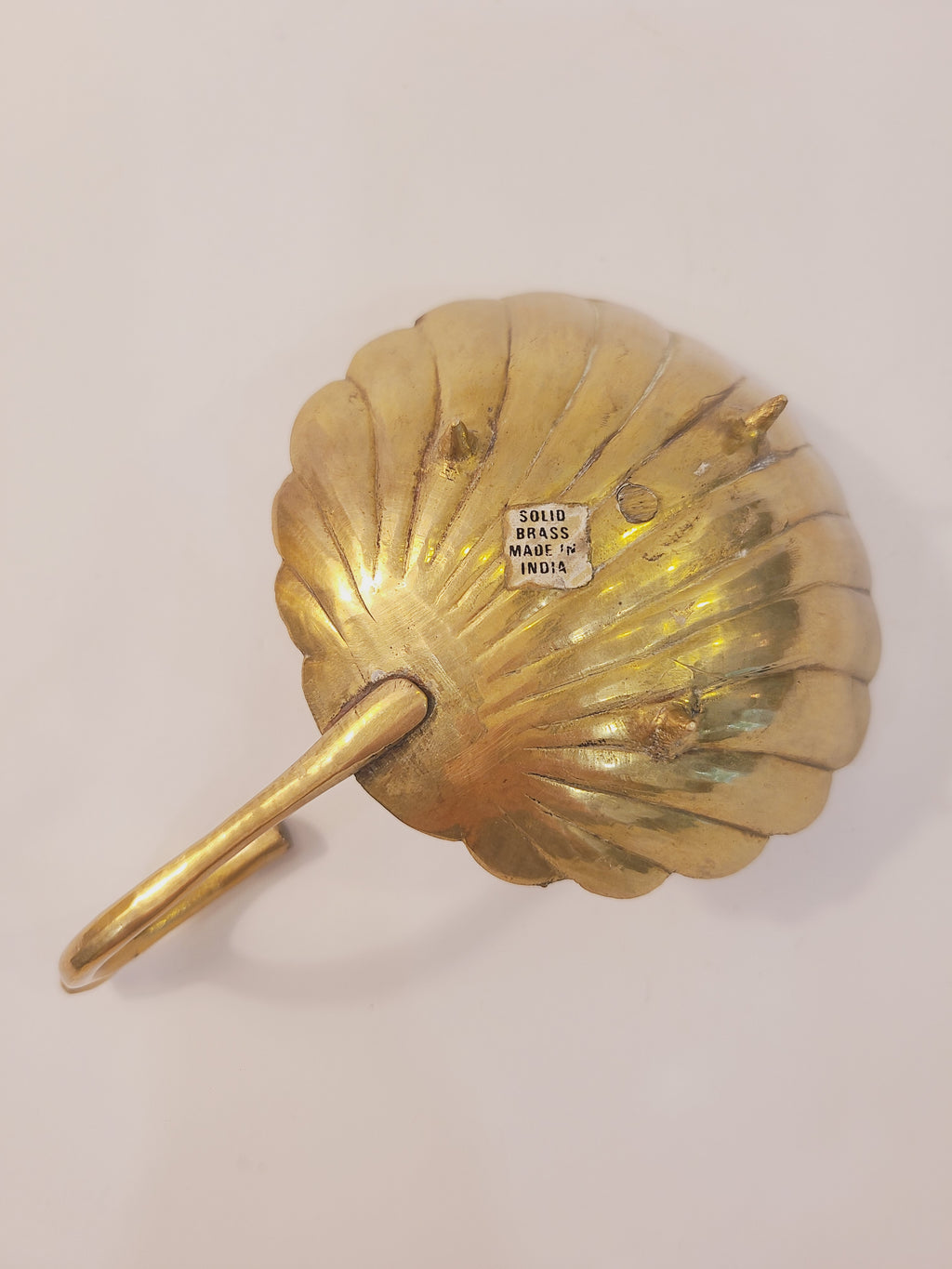 Underside of brass shell chamber candlestick showing Solid Brass Made in India label and reverse scallop shell relief, vintage coastal candle holder