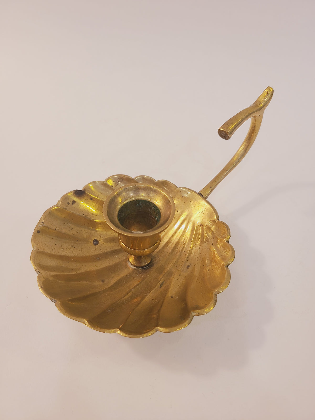 Top-down view of solid brass scallop shell chamber candle holder showing radiating shell ribs, taper cup, and finger loop handle, vintage coastal decor