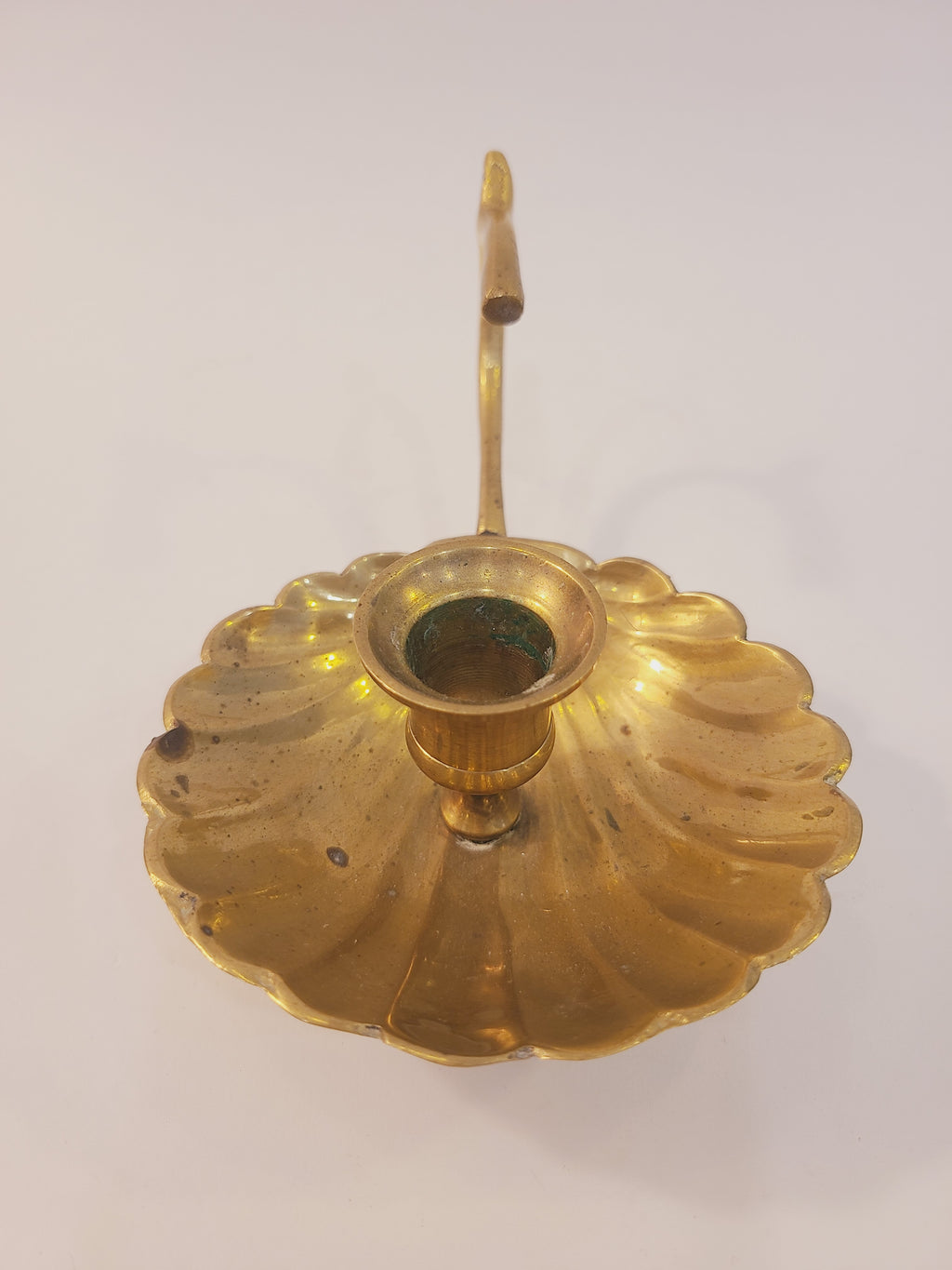 Front view of brass shell motif chamber candlestick, scalloped saucer with centered taper cup and upright finger loop handle, 4 inch solid brass