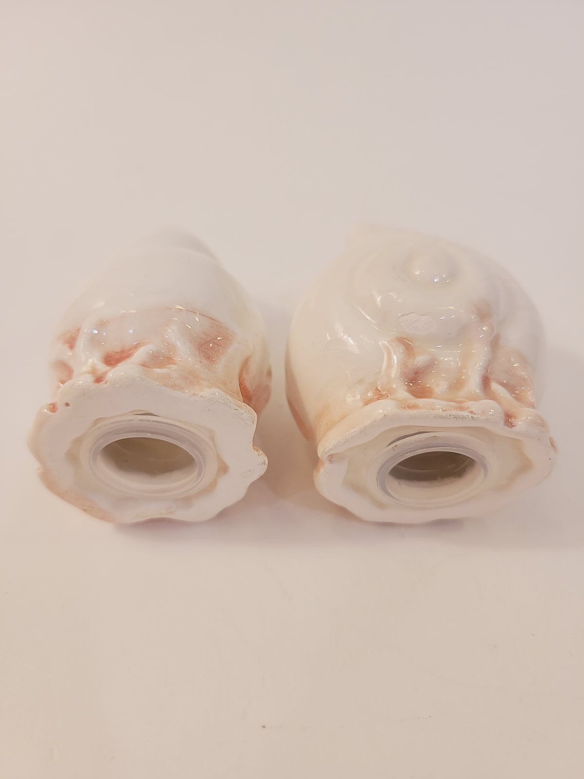 Underside of Fitz and Floyd Coquille seashell salt and pepper shakers showing open plug holes and scalloped pink coral base molding, vintage ceramic coastal set