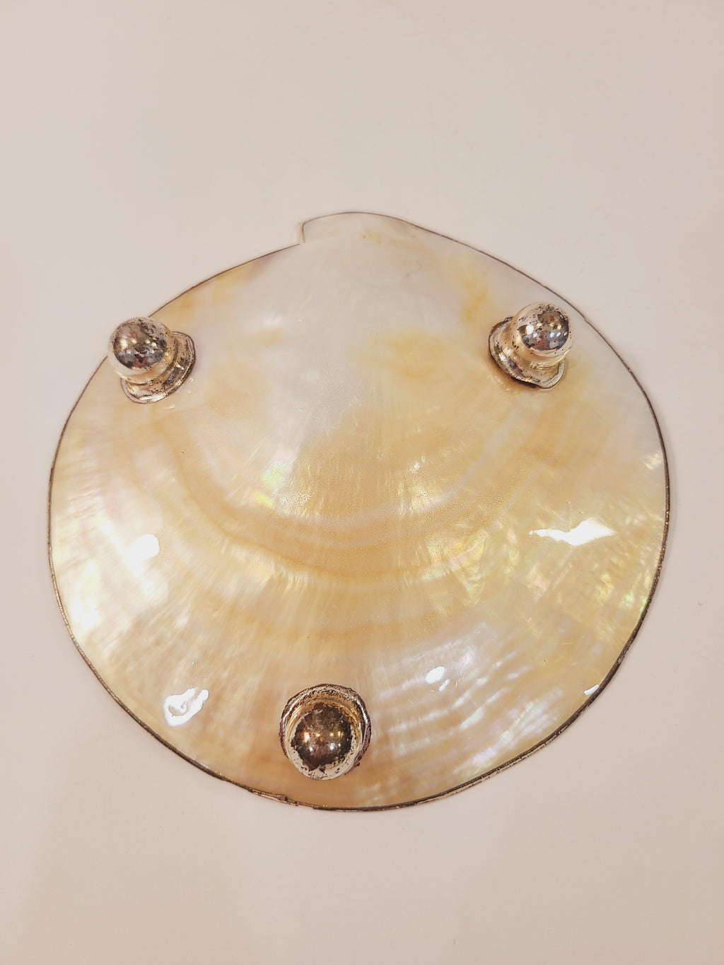 Underside of vintage mother of pearl dish showing three silver metal ball feet and iridescent nacre shell exterior, 6 inch footed dish
