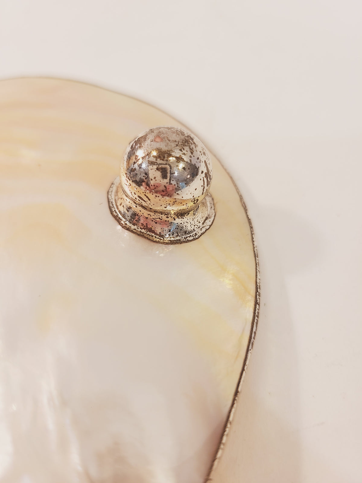 Close-up of distressed silver metal ball foot on vintage mother of pearl dish showing authentic age patina and wear, vintage coastal decor