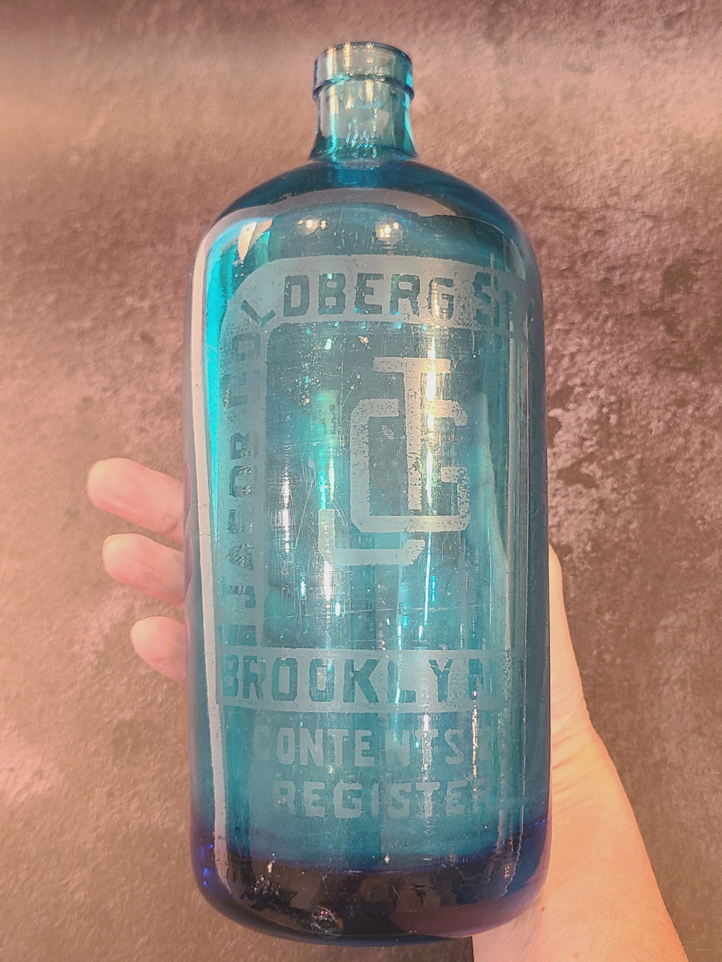 Close-up of etched Jacob Goldberg Seltzer Distributor lettering on a turquoise glass bottle