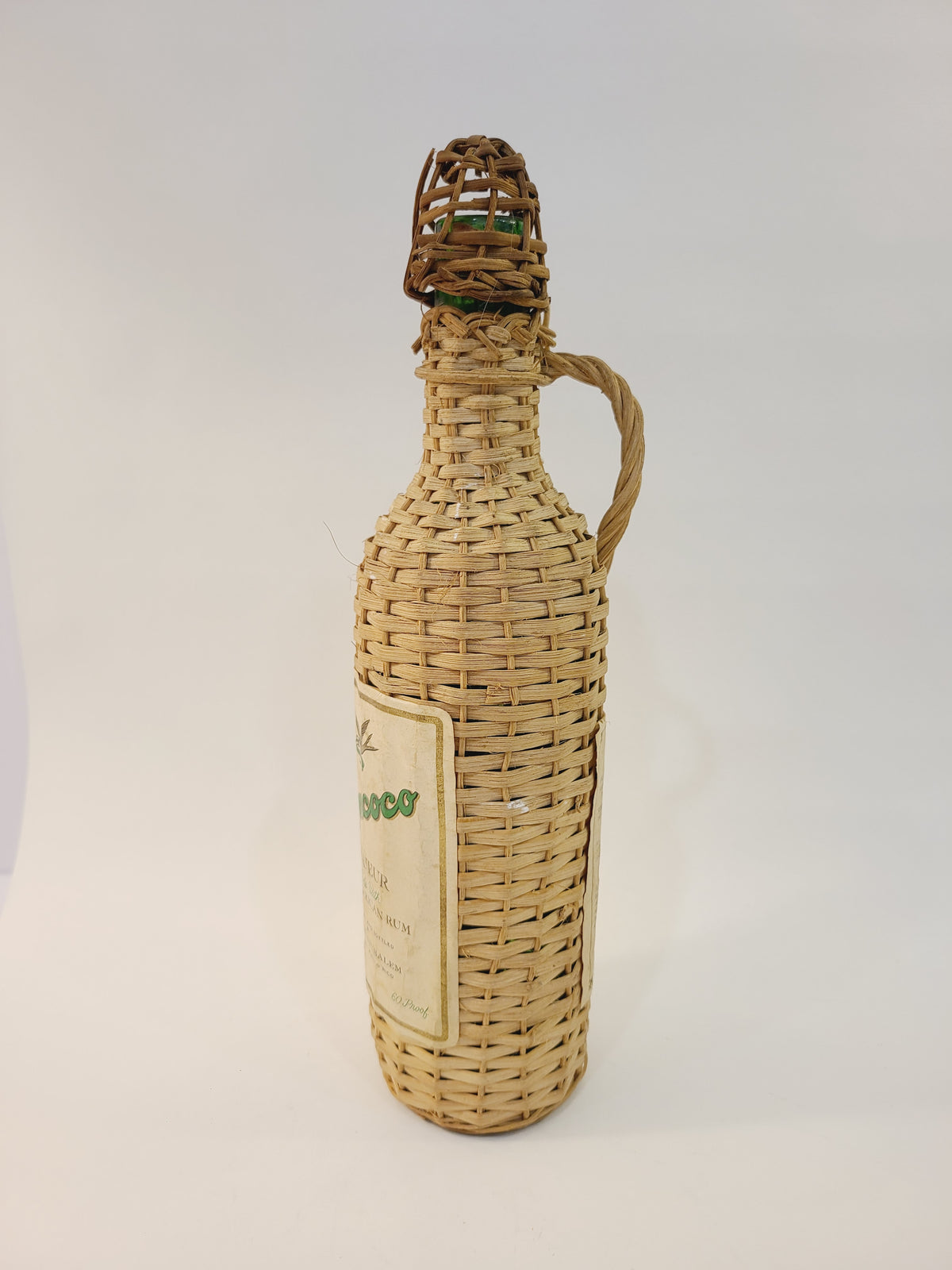 Roncoco wicker-wrapped rum bottle side view showing rattan handle and woven casing, vintage coastal or tiki bar decor