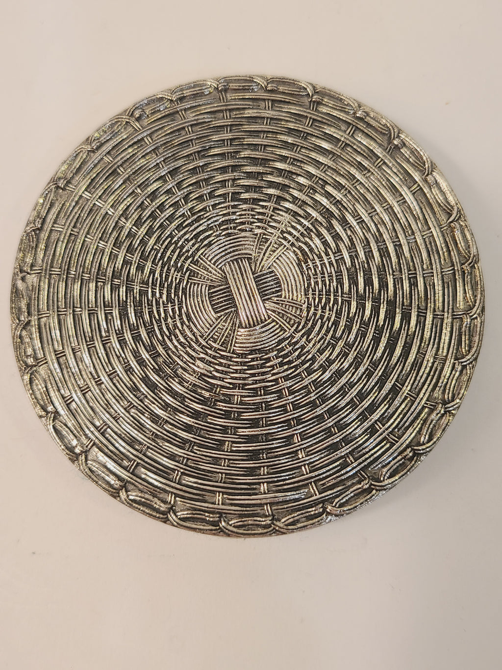 Close-up of single mid-century woven metal drink coaster showing tight circular basketweave and polished silver finish with age patina