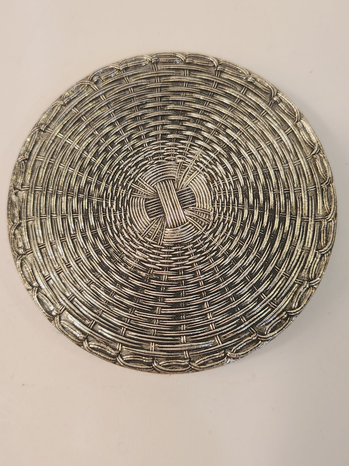 Close-up of single mid-century woven metal drink coaster showing tight circular basketweave and polished silver finish with age patina