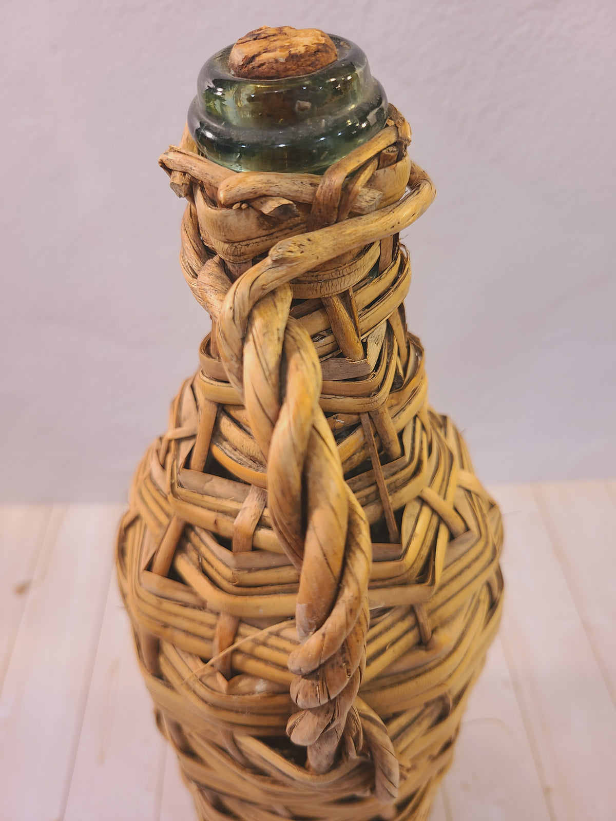 Close-up of the original cork stopper and pale green glass neck on a rattan-wrapped demijohn
