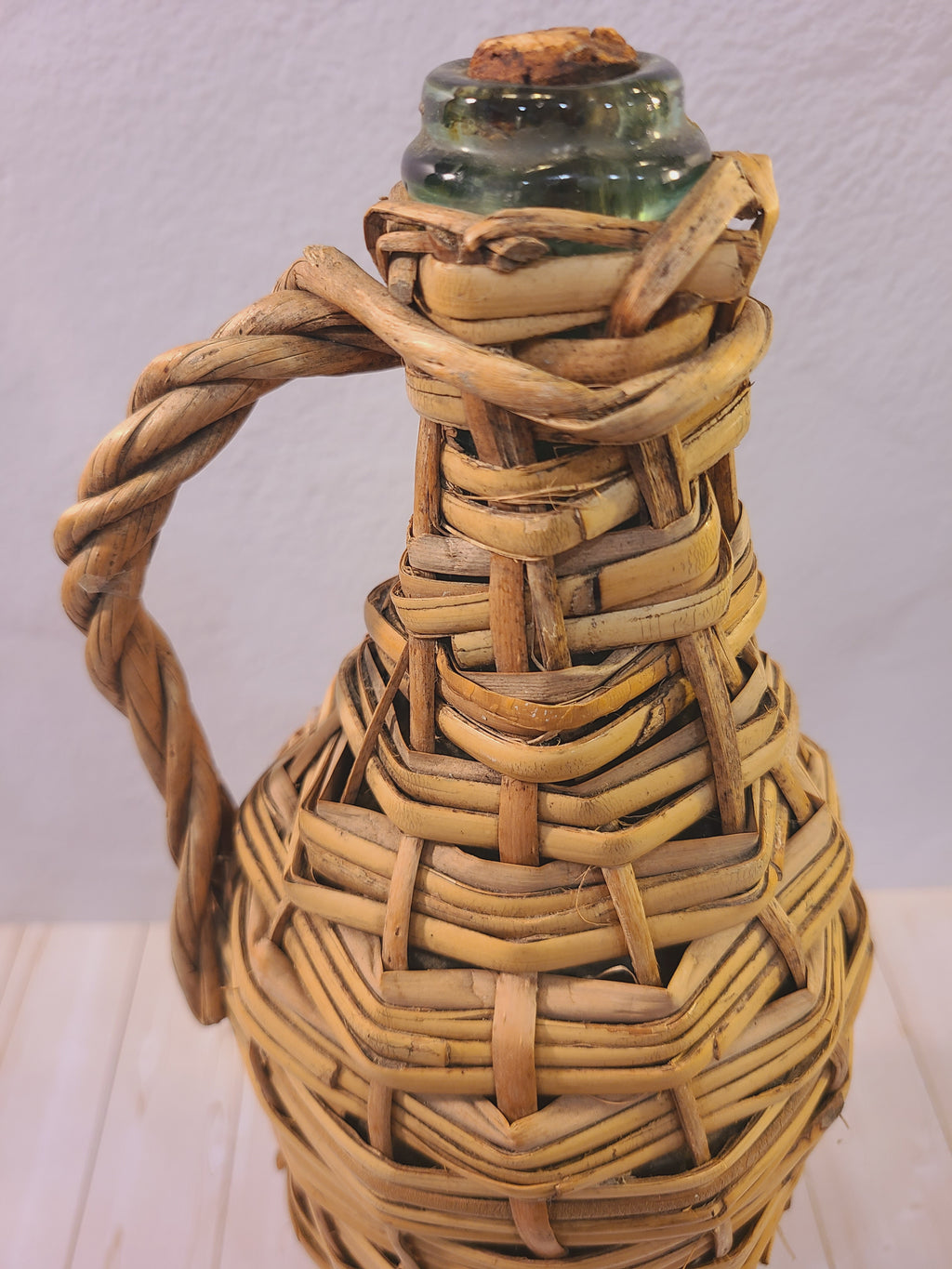 Close-up of the original cork stopper and pale green glass neck on a rattan-wrapped demijohn