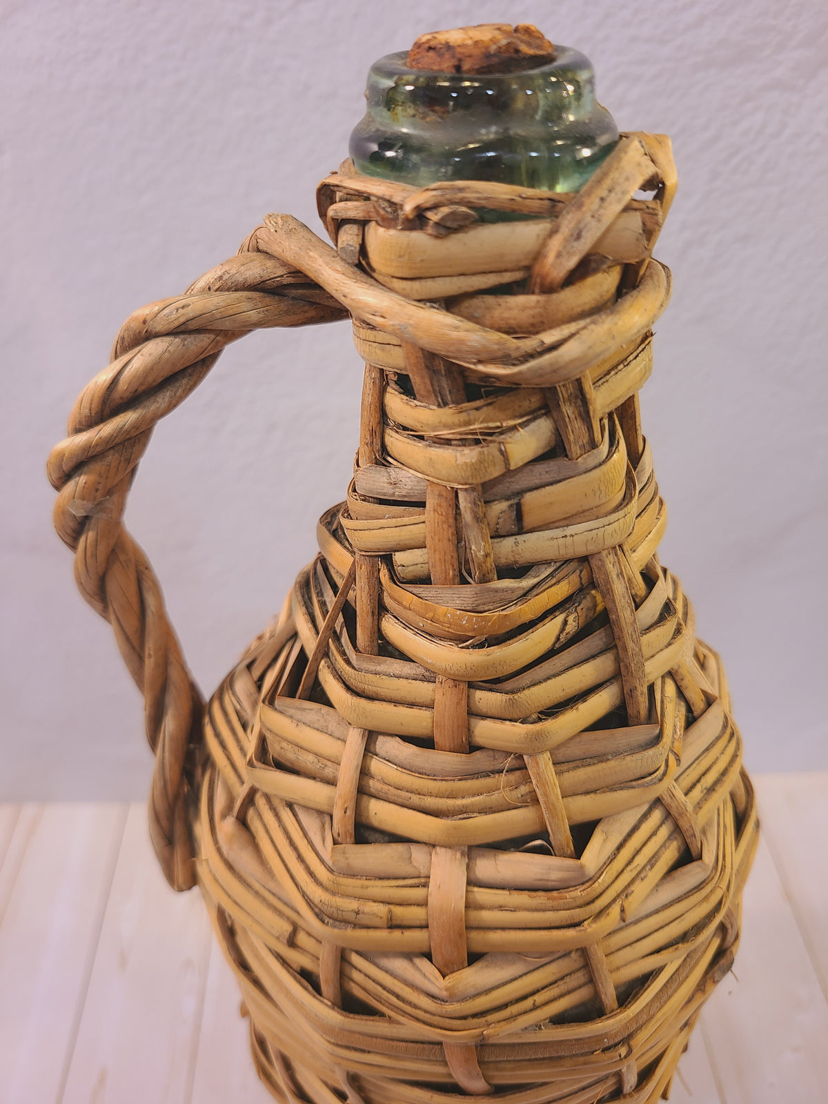 Close-up of the original cork stopper and pale green glass neck on a rattan-wrapped demijohn