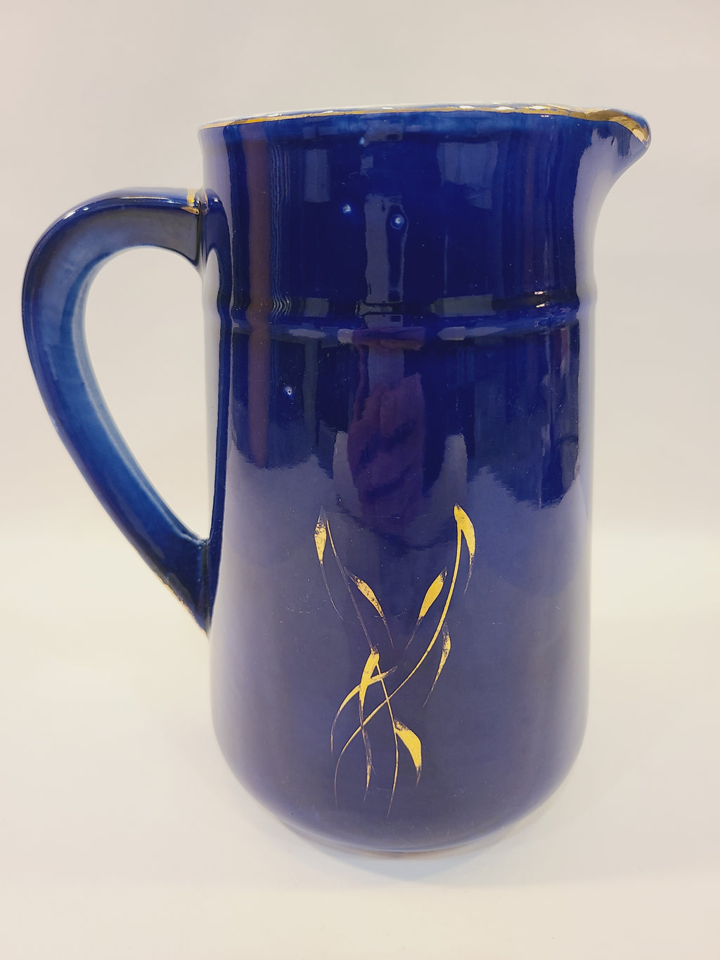 Reverse side of a cobalt blue pitcher showing gold foliage accents and curved handle