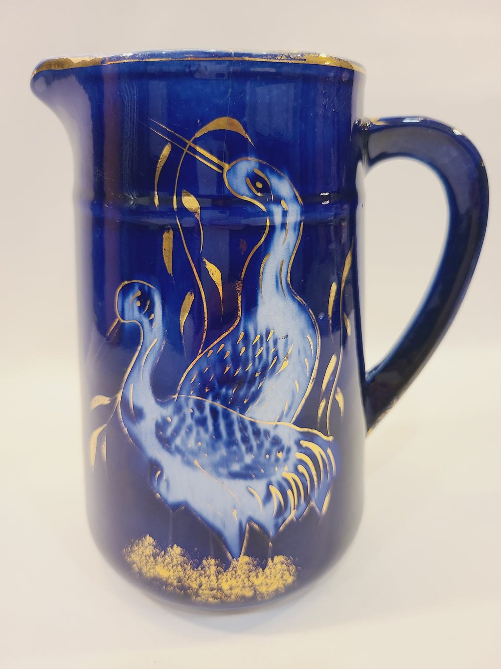 Close-up of two cranes and gold foliage painted on a cobalt blue ceramic pitcher