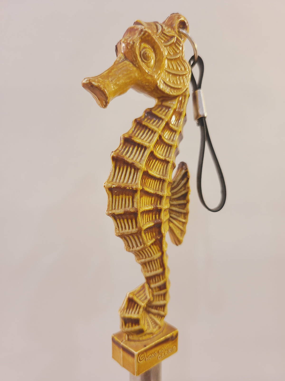 Close-up of tan seahorse-shaped handle with textured fins, curled tail, and Carrib maker mark