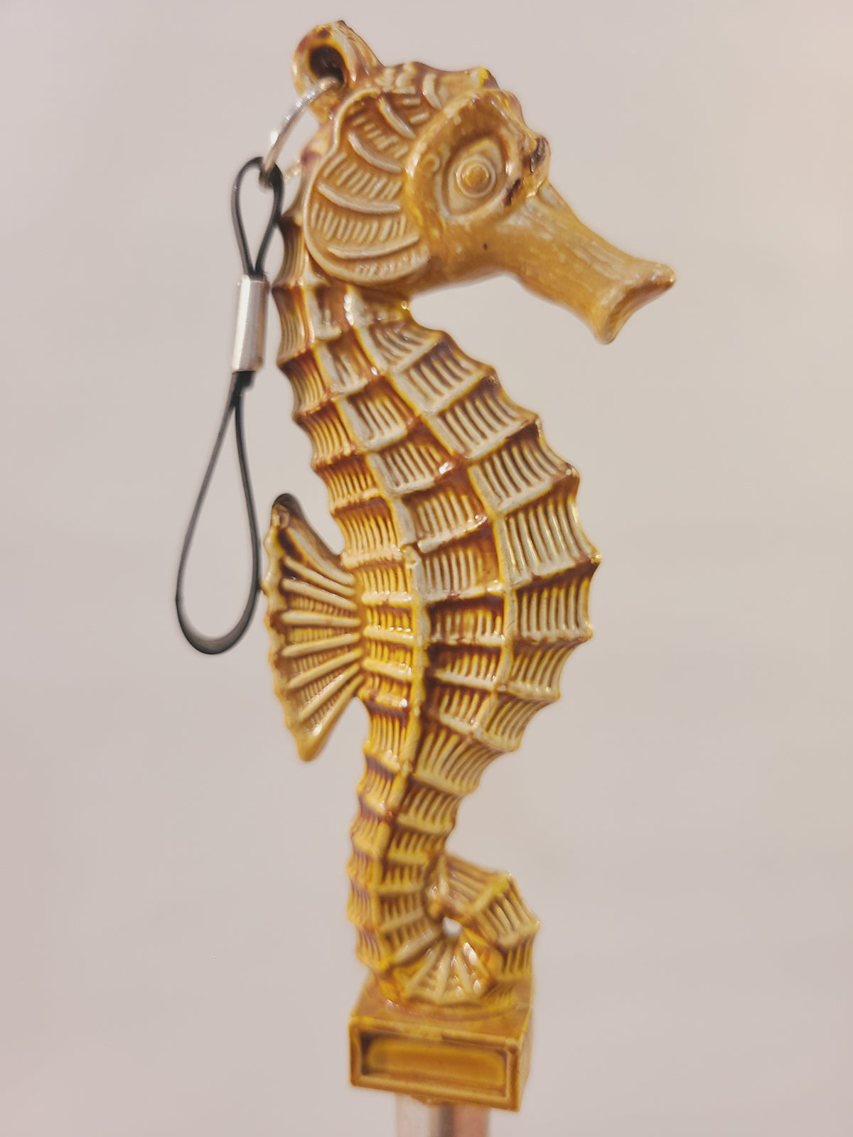 Side view of a tan seahorse clothes brush with textured fins, decorative tail, and hanging loop