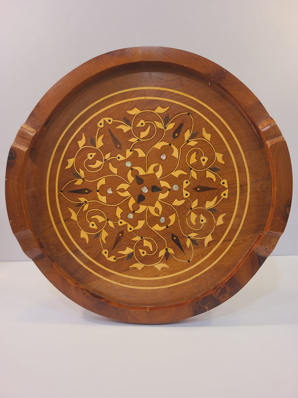 Round vintage inlaid wood serving tray with botanical scrollwork, mother-of-pearl accents, raised rim, and carved handles