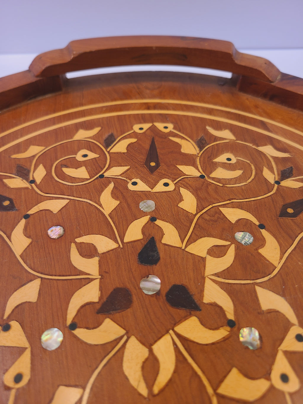 Detail of scrolling vine inlay, stylized leaves, and mother-of-pearl discs on a wood tray