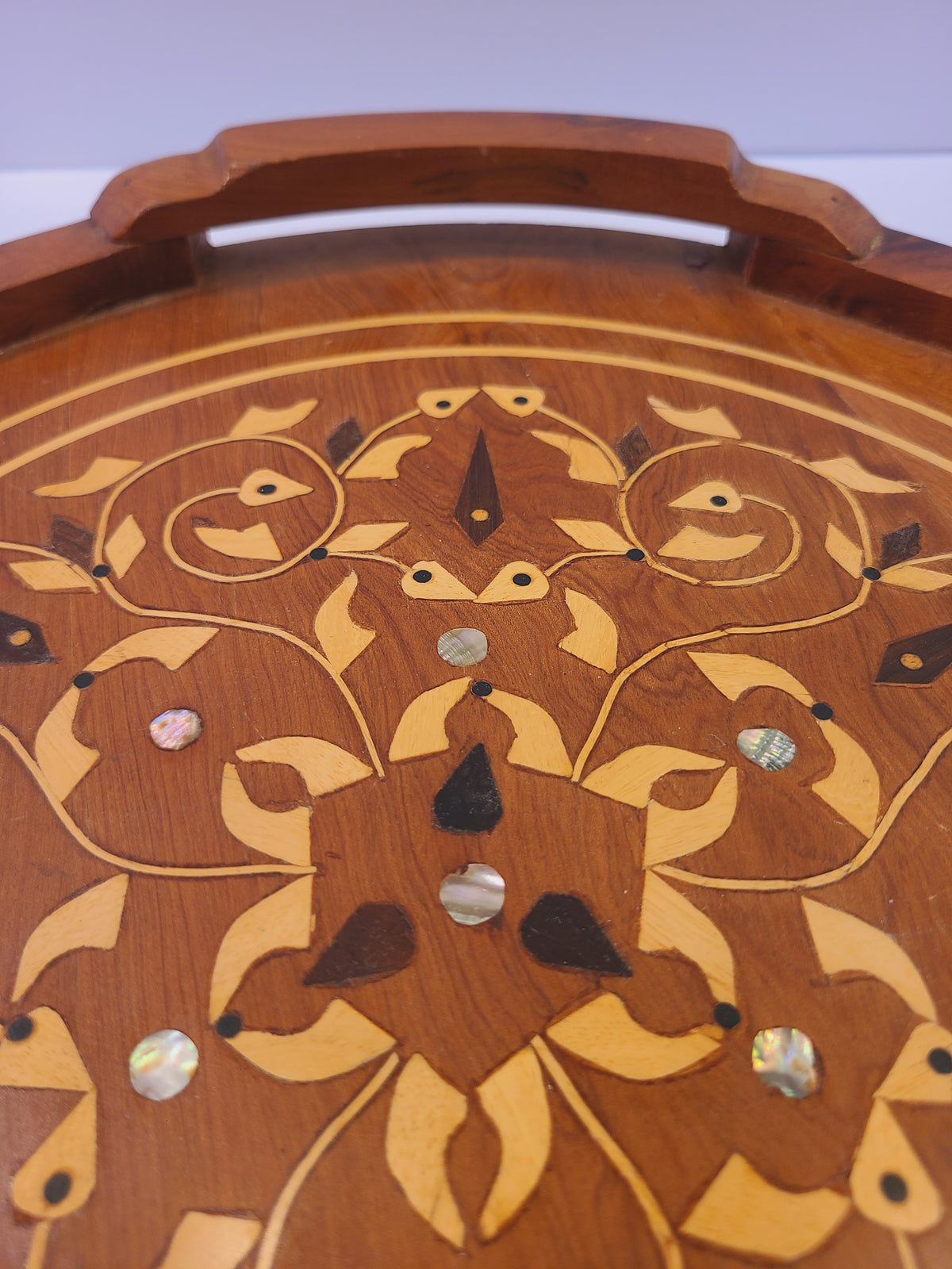 Detail of scrolling vine inlay, stylized leaves, and mother-of-pearl discs on a wood tray
