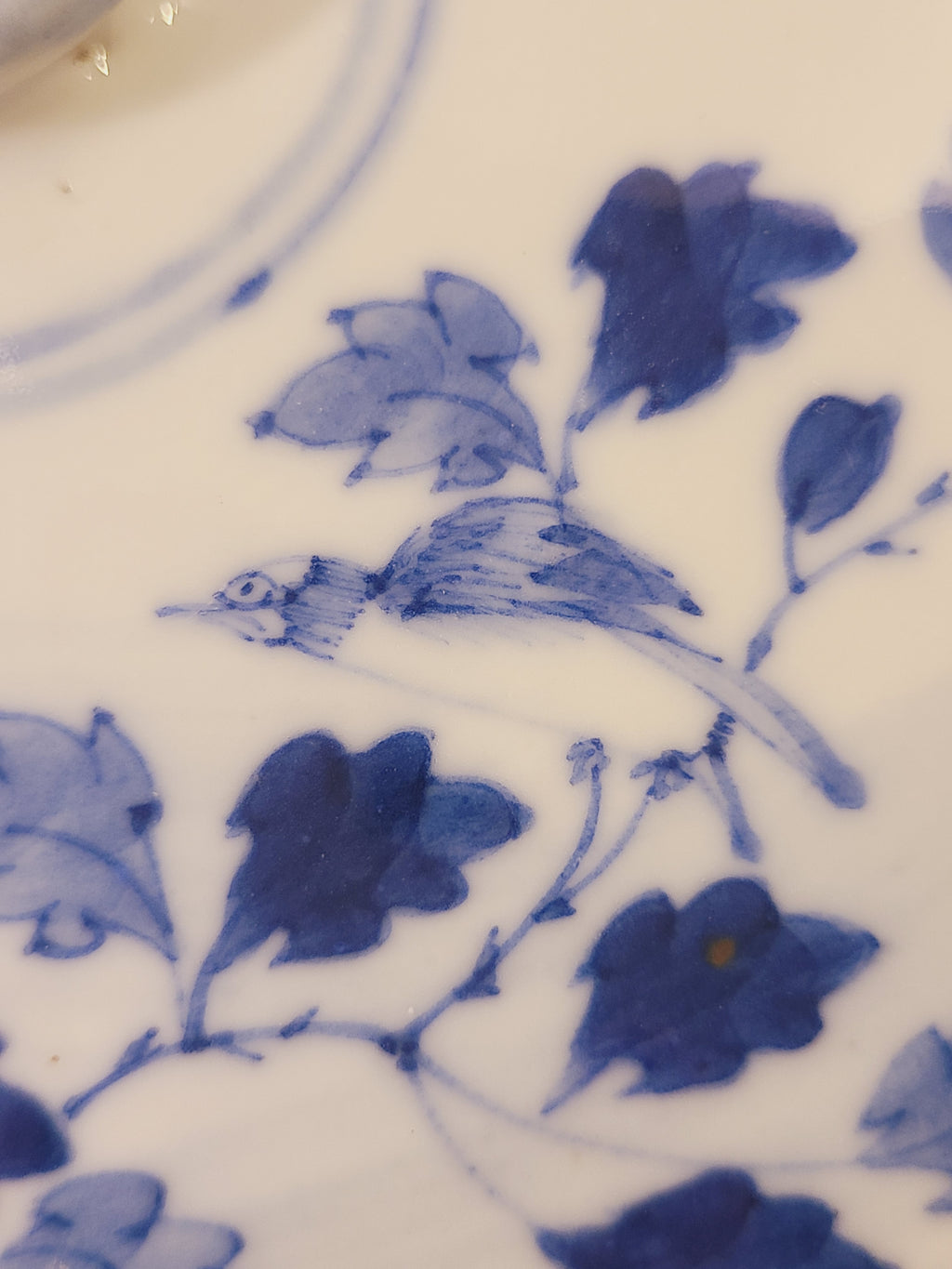 Close-up of hand-painted East Asian cobalt blue bird and floral decoration on a white porcelain serving bowl