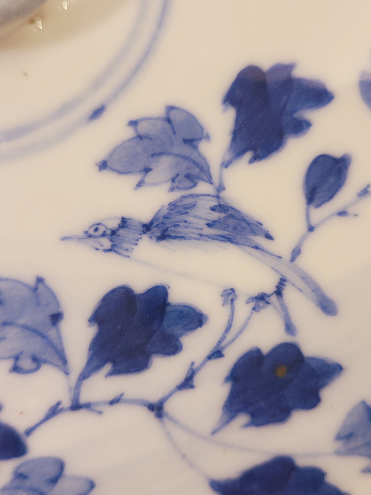 Close-up of hand-painted East Asian cobalt blue bird and floral decoration on a white porcelain serving bowl